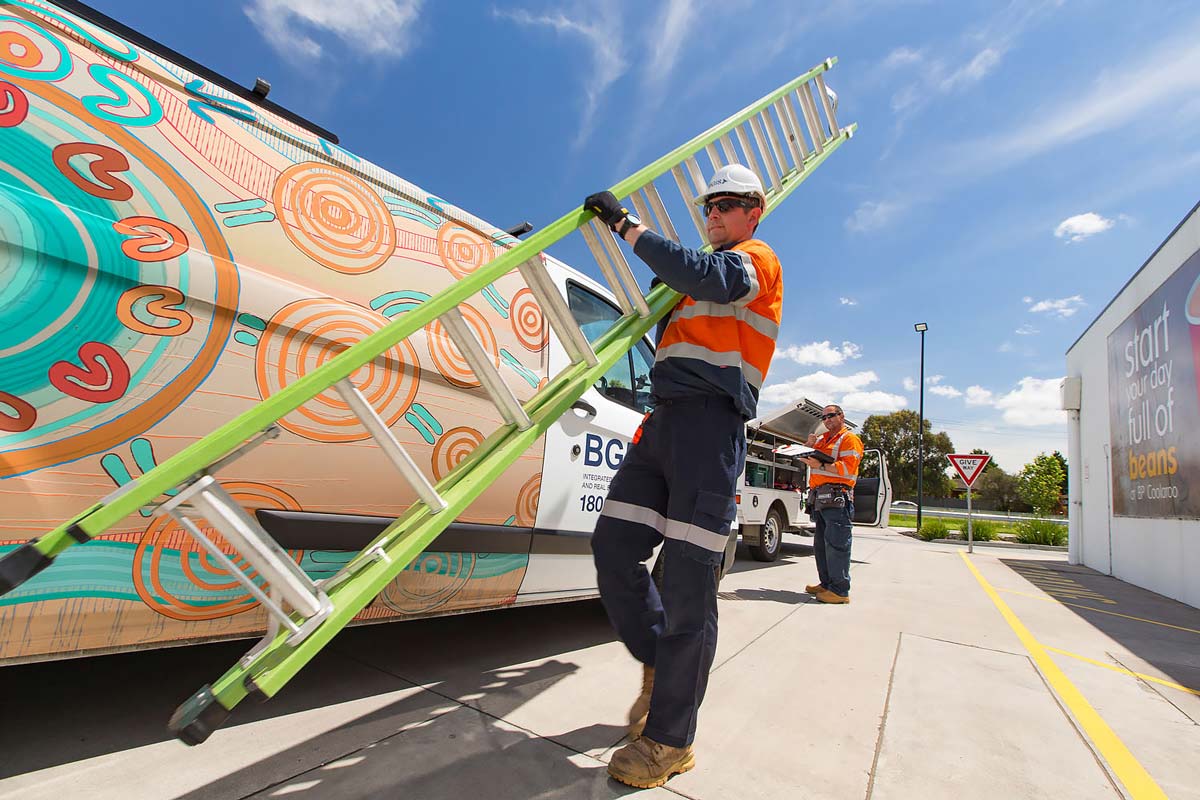 BGIS Employee holding a ladder next to a van with BGIS branding