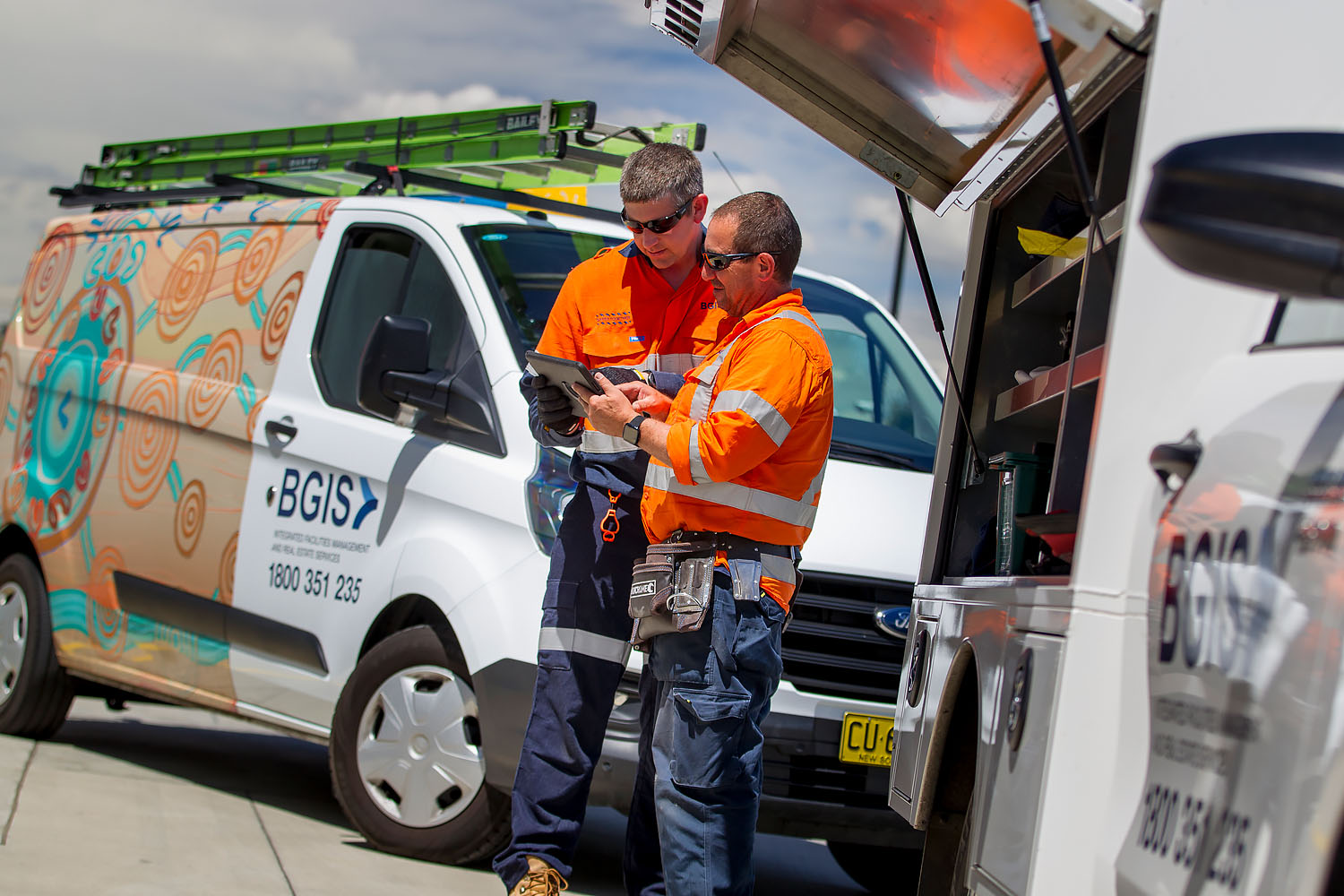 two trades people standing by their vehicles looking at an ipad