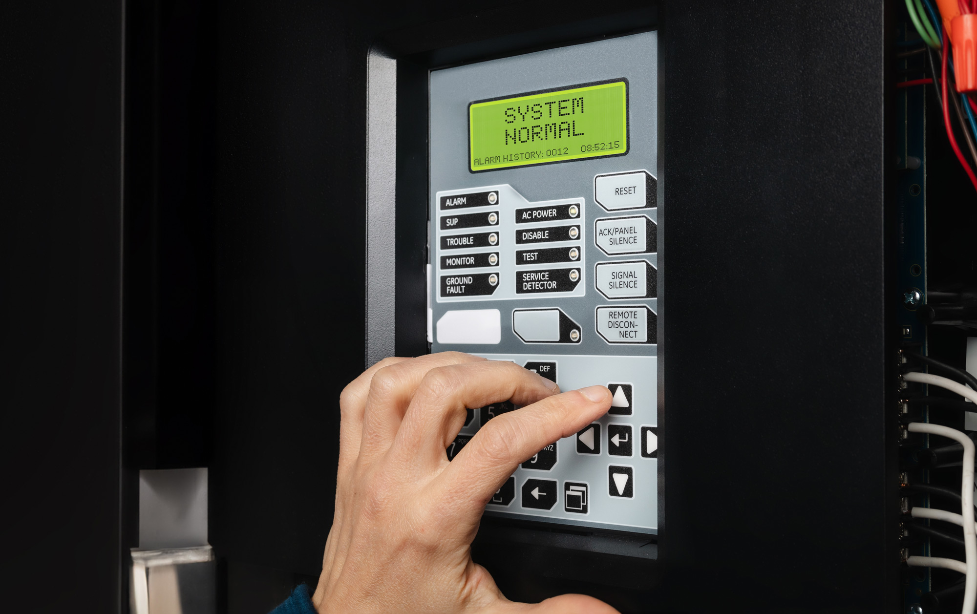 Technician using fire alarm control panel in service room.